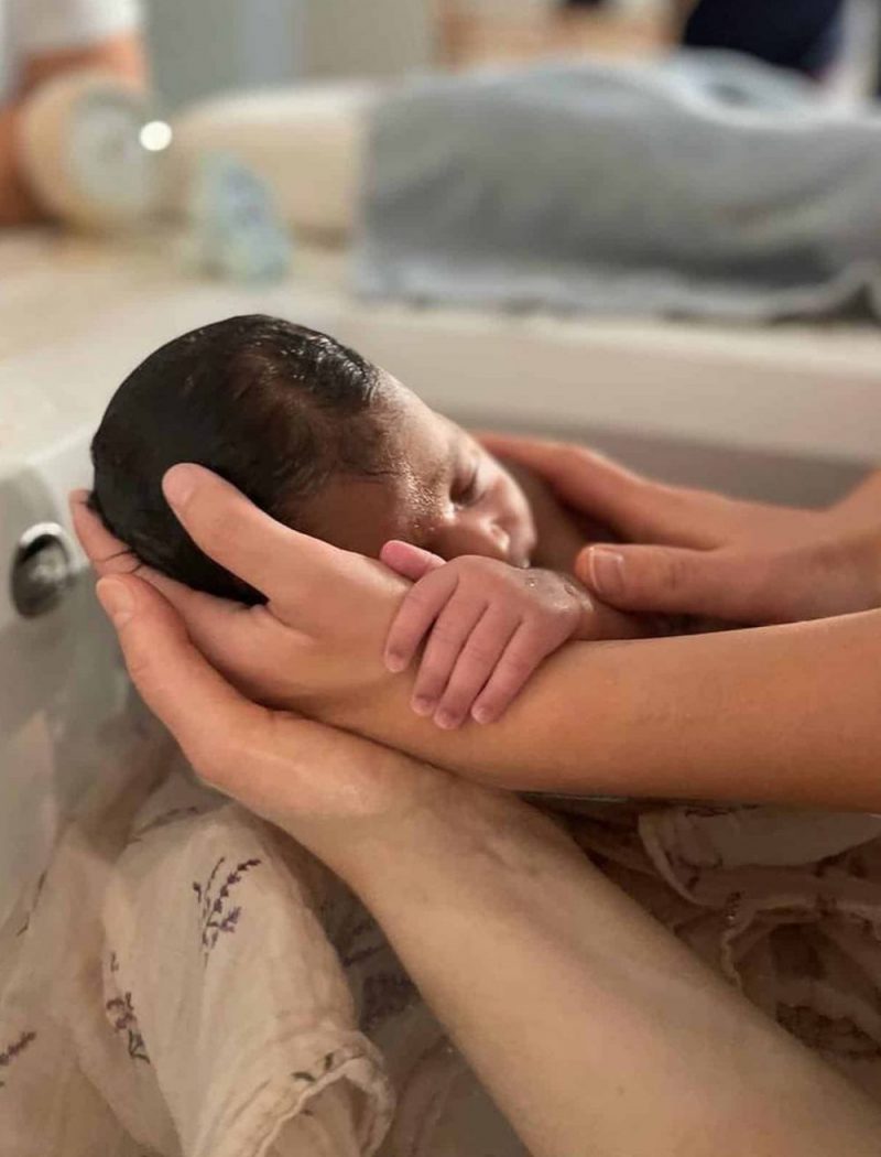 baby being washed in bath by hands